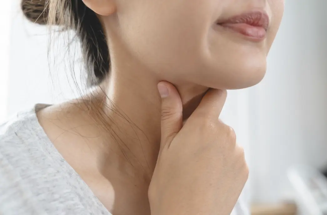 Woman touching her throat due to hoarseness associated with vocal cord paralysis.